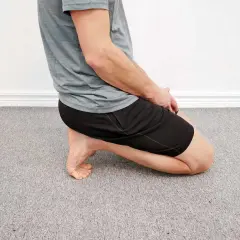 Man utför en soleus stretch på ett grått heltäckningsgolv.