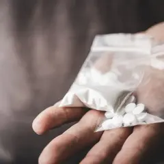 En hand håller en plastpåse med vitt pulver och flera vita tabletter, kanske anafranil dropp.