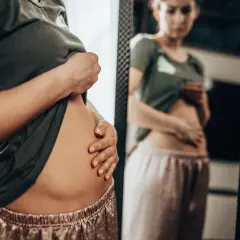 Kvinna känner på sin uppblåsta mage, en vanlig symtom vid IBS. Inulin kan vara en lösning.