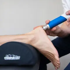 Behandling med stötvåg för att lindra smärta vid plantar fasciit. En blå enhet används på hälen.