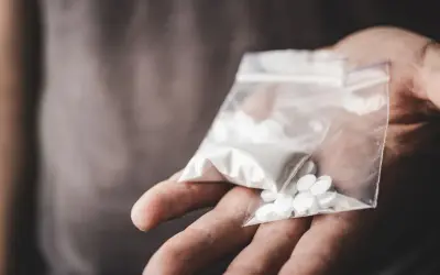 En hand håller en plastpåse med vitt pulver och flera vita tabletter, kanske anafranil dropp.
