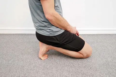 Man utför en soleus stretch på ett grått heltäckningsgolv.