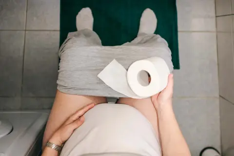 Gravid kvinna med hård i magen sitter på toaletten med en rulle toalettpapper.