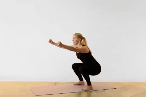 Kvinna utför en sumo squat på en träningsmatta.
