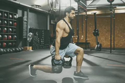 Man utför utfall med kettlebells under ett intensivt crossfit pass i ett modernt gym.