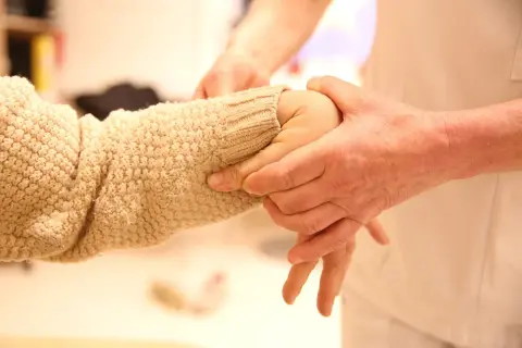 En person undersöker en arm med stickad tröja, möjligen för att bedöma ehlers danlos syndrom symtom som överrörlighet.