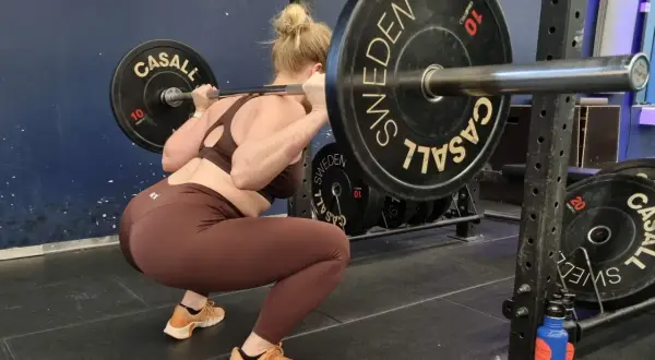 Kvinna utför squats med vikt. Stången vilar på hennes axlar, med viktskivor märkta "Casall Sweden".
