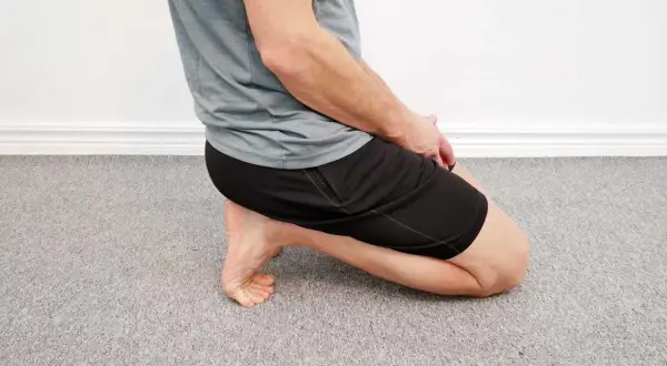Man utför en soleus stretch på ett grått heltäckningsgolv.