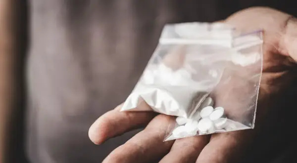 En hand håller en plastpåse med vitt pulver och flera vita tabletter, kanske anafranil dropp.