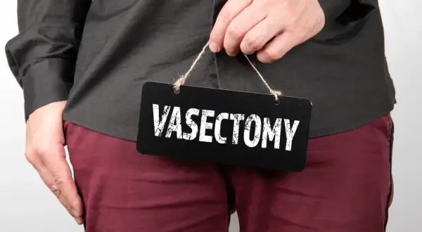 A person holds a black sign with "VASECTOMY" written in white text.
