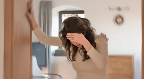 Kvinna håller sig mot en dörrkarm, ansiktet dolt av handen, upplever yrsel efter måltid.