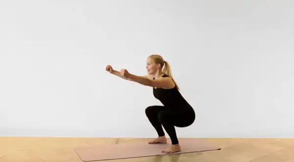 Kvinna utför en sumo squat på en träningsmatta.