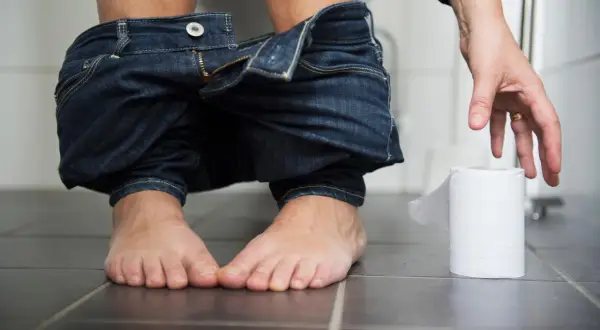 En person sitter på toaletten med neddragna jeans. En hand sträcker sig efter en rulle toalettpapper. Frågan "hur ofta ska man bajsa" dyker upp.