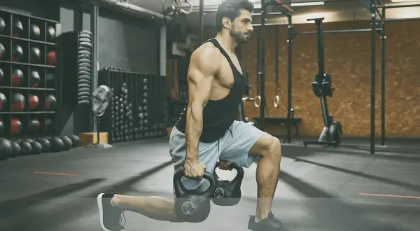 Man utför utfall med kettlebells under ett intensivt crossfit pass i ett modernt gym.