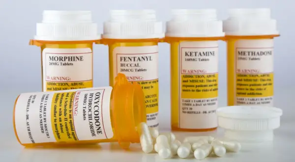 Flera medicinburkar med starka läkemedel som morfin, fentanyl och oxykodon. En burk med oxykodon ligger ner med kapslar utspridda. Dessa är exempel på snabbverkande morfin och liknande preparat.