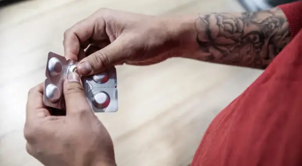 Händer med tatueringar öppnar en tablettask, kanske med naproxen och alvedon för att lindra smärta.