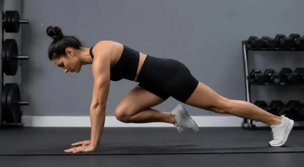 Kvinna utför mountain climbers på en träningsmatta i ett gym.