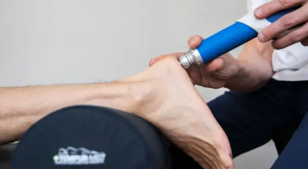 Behandling med stötvåg för att lindra smärta vid plantar fasciit. En blå enhet används på hälen.