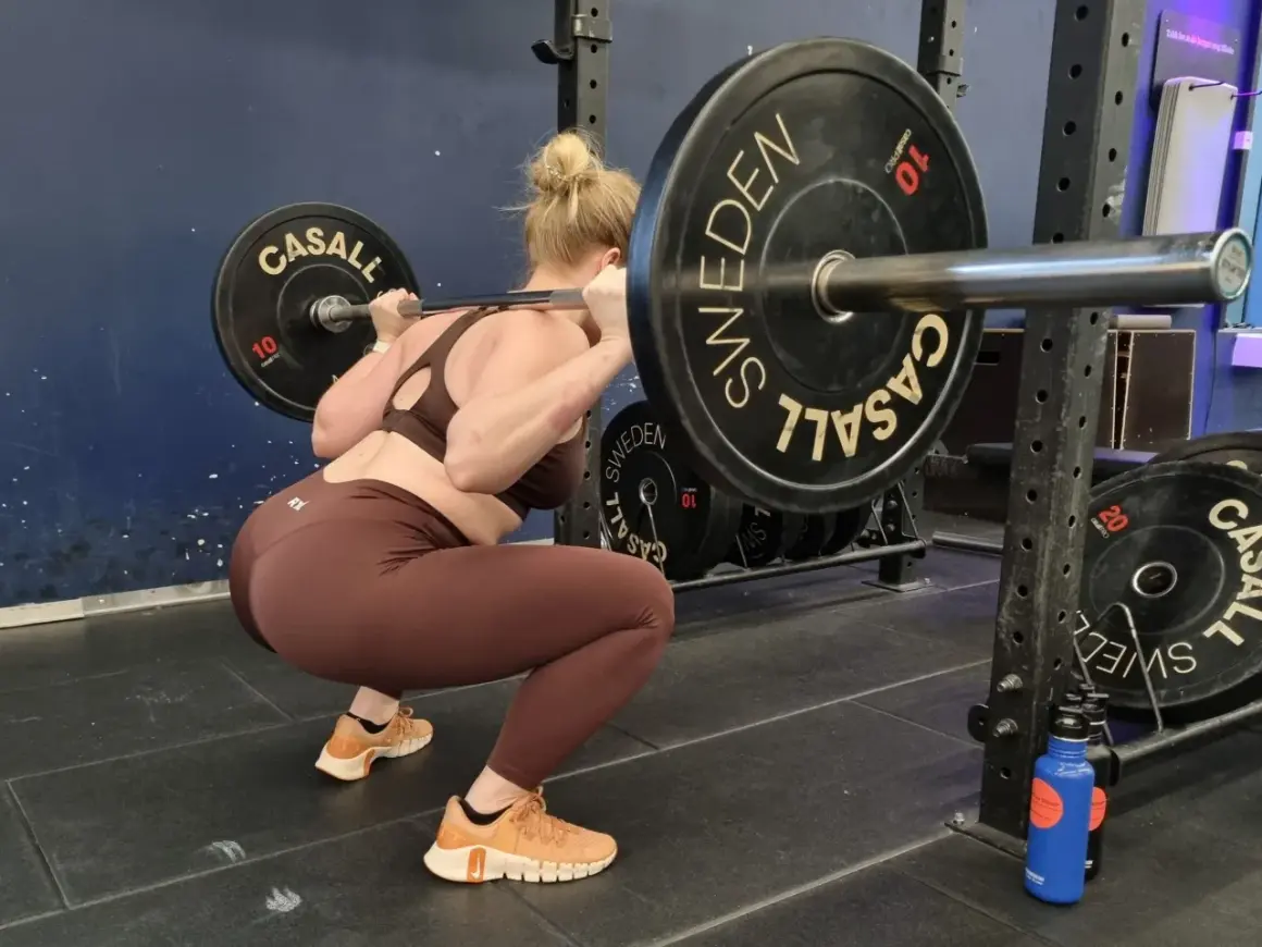 Kvinna utför squats med vikt. Stången vilar på hennes axlar, med viktskivor märkta "Casall Sweden".