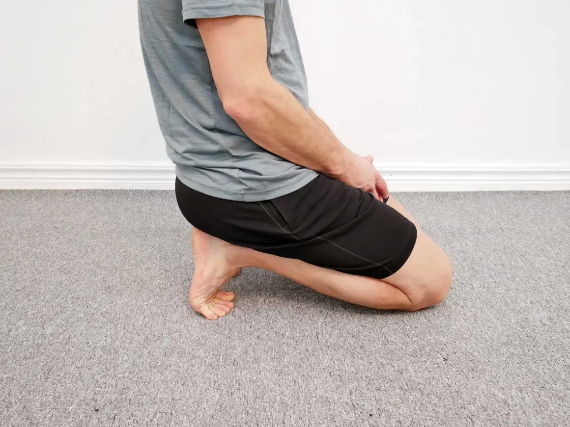 Man utför en soleus stretch på ett grått heltäckningsgolv.