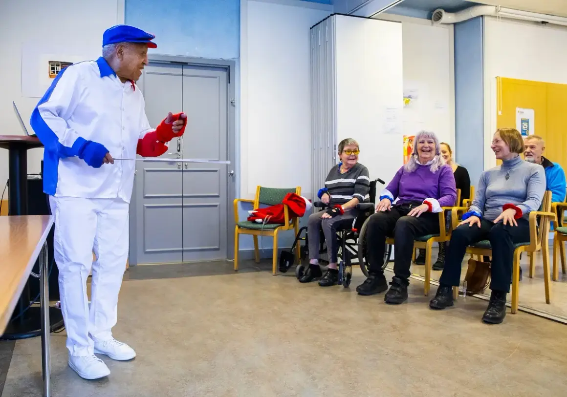 Man i vit dräkt leder en grupp äldre i en Ronnie Gardiner Method-övning.