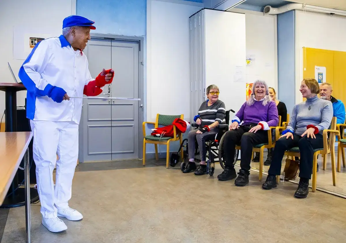 Man i vit dräkt leder en grupp äldre i en Ronnie Gardiner Method-övning.
