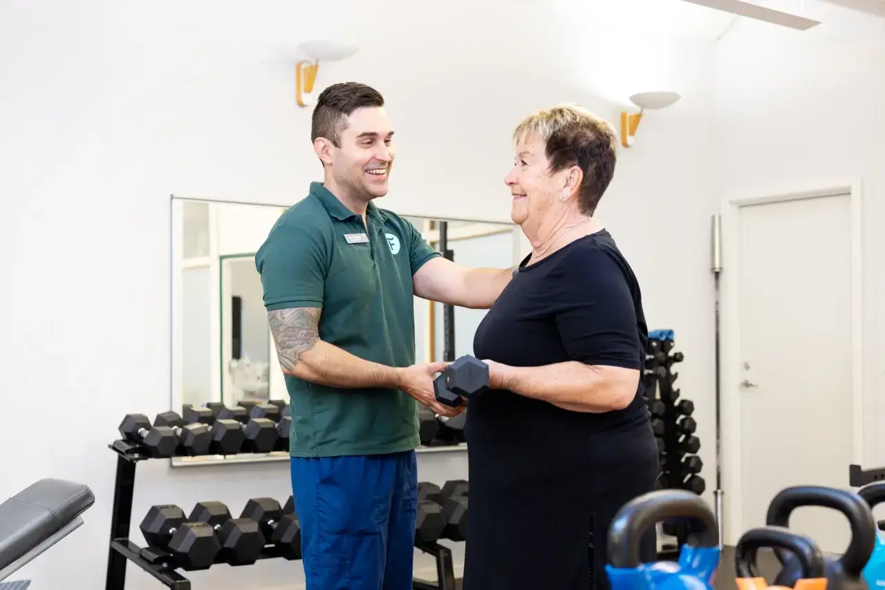 Fysioterapeut friskv&aring;rd hj&auml;lper en &auml;ldre kvinna med vikter i ett gym.