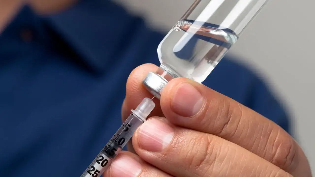 Närbild på en hand som drar upp biologisk medicin i en spruta från en ampull.