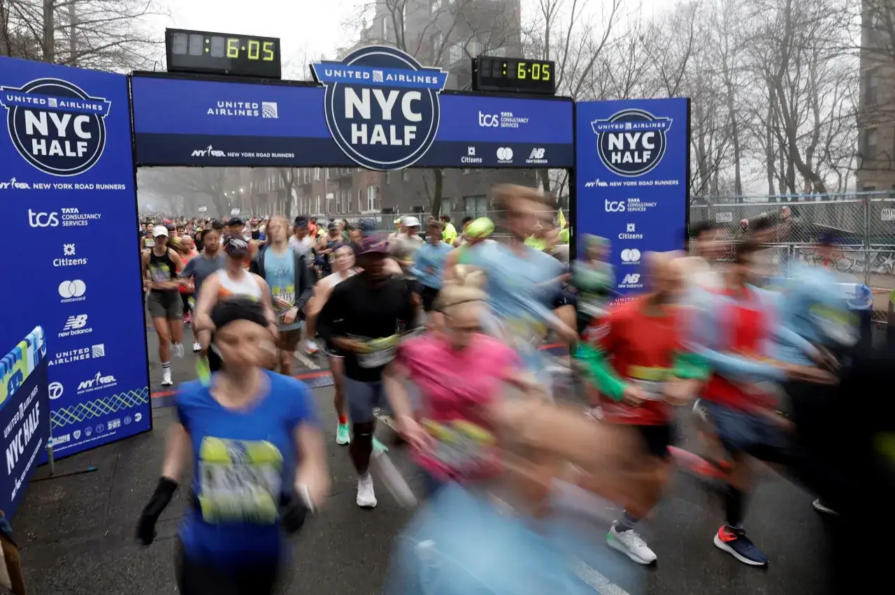 Löpare rusar förbi målgången för NYC Half. Klockan visar 6:05, kanske en tid för en negativ split.