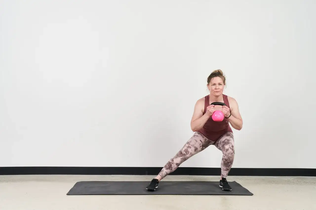 Kvinna utför utfall med kettlebell, en variant av squats svenska.