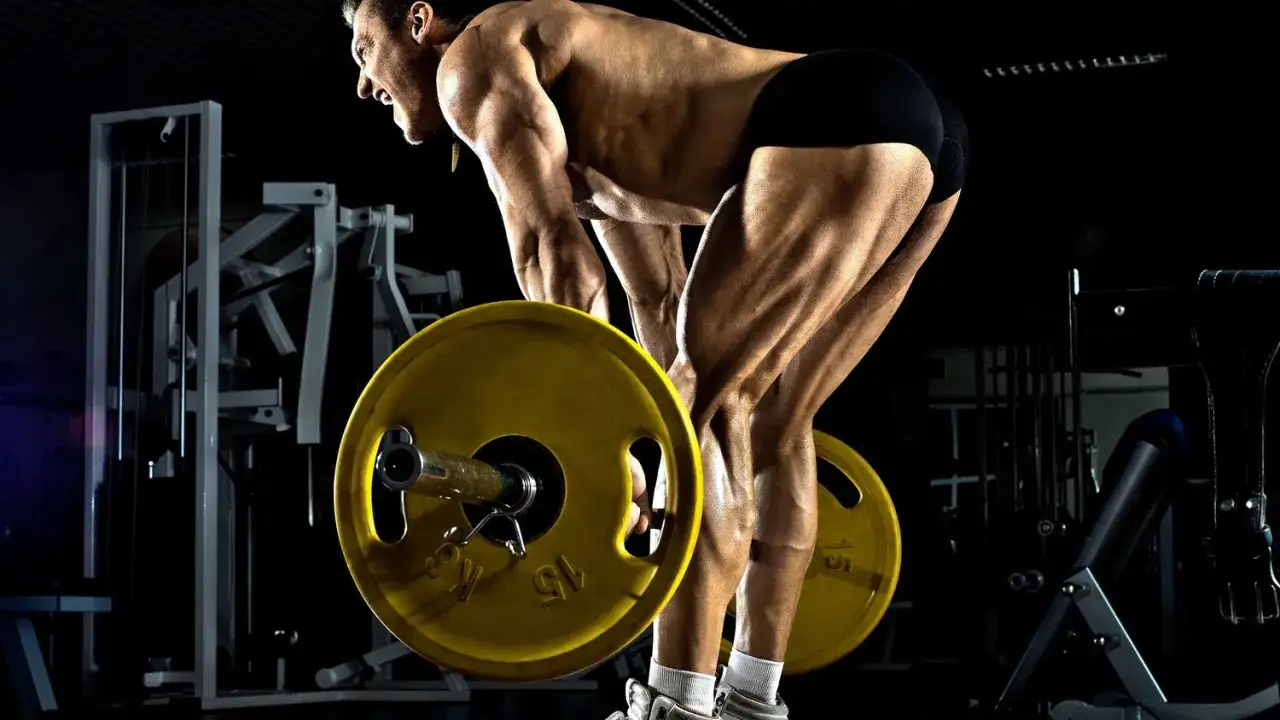 Muskulös man utför en romanian deadlift med en skivstång i ett gym.