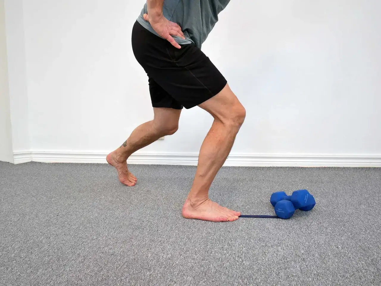 Man med artros i fotleden utför rehabövning med gummiband och hantlar.