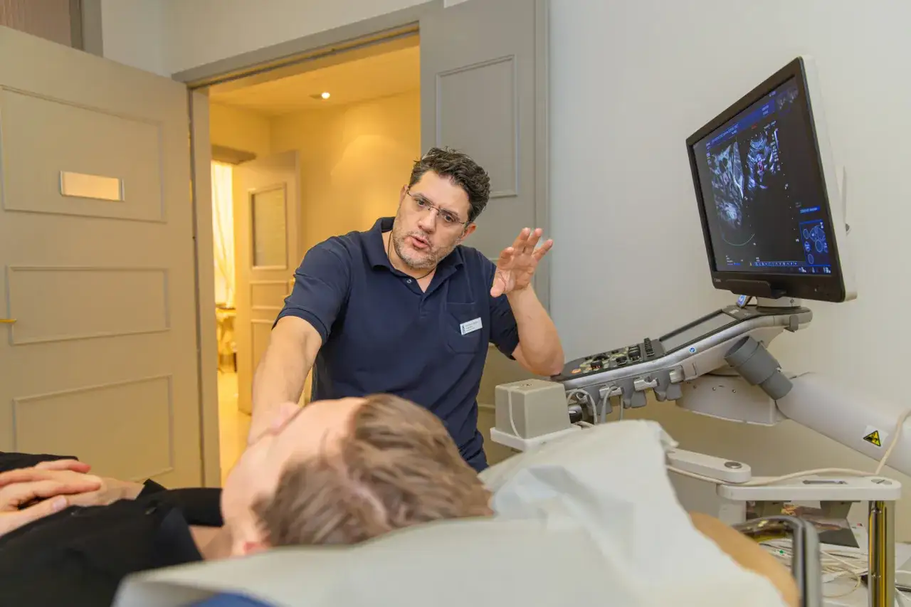 Läkare förklarar nervblockad vid ultraljudsapparat. Patienten ligger på britsen.