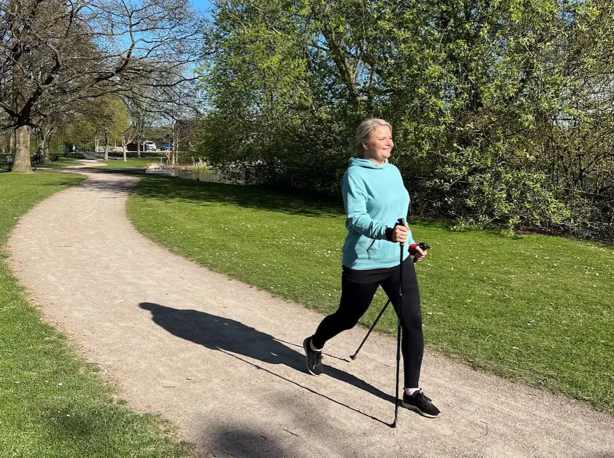 Kvinna med stavar p&aring; en grusv&auml;g i en park, &ouml;var p&aring; sin stavg&aring;ng teknik.