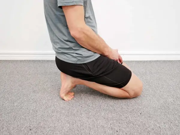 Man utför en soleus stretch på ett grått heltäckningsgolv.