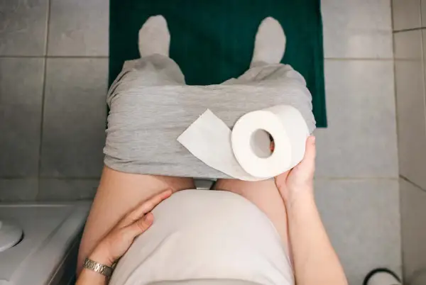 Gravid kvinna med hård i magen sitter på toaletten med en rulle toalettpapper.