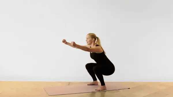 Kvinna utför en sumo squat på en träningsmatta.