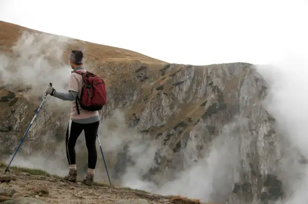 Vandrare med stavar, redo att utforska bergsterräng med moln som sveper in. Stavgång teknik är nyckeln för att navigera i denna utmanande miljö.