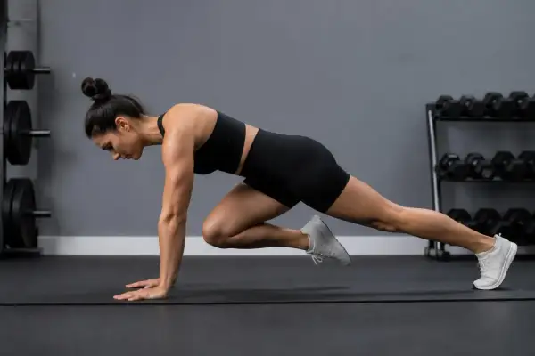 Kvinna utför mountain climbers på en träningsmatta i ett gym.